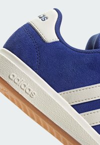 Blå mockaskor med vita läderdetaljer och tre ränder. Strukturerad gummisul med ett greppmönster. Logotyp på hälen.