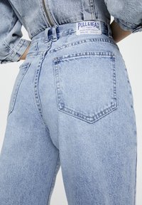 Vaqueros de denim azul claro con una cintura alta, dos bolsillos traseros y una etiqueta de marca en la cinturilla. La tela tiene un acabado texturizado.
