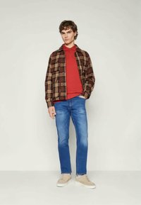 Pruun ja pruunikirjuline särk punase polo, millele on kombineeritud heledatest sinistest teksadest ja beežidest tossudest. Mudel seisab neutraalses taustas.