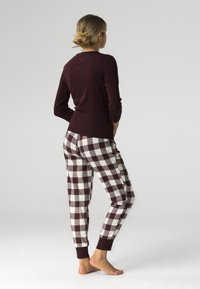 Maroonowy, długi rękaw bluzki zestawiony z białymi i bordowymi w kratkę spodniami do piżamy. Miękka tkanina z prążkowanymi mankietami przy kostkach.