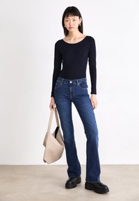 Marineblauwe lange mouw top, uitlopende blauwe spijkerbroek, zwarte plateau schoenen en een beige tote bag. Eenvoudig ontwerp en klassieke kleurenpalet.