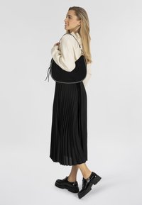 Sac en cuir suédé noir avec des accents en clous argentés, de forme décontractée et une bandoulière. Porté avec une longue jupe plissée noire et des chaussures à plateforme.