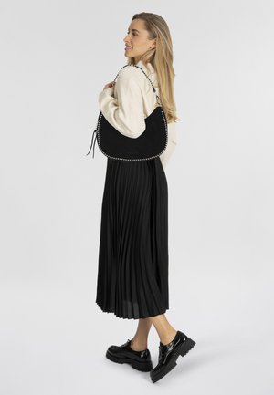 Borsa a tracolla in suede nero con dettagli in argento, forma morbida e tracolla. Indossata con una lunga gonna plissettata nera e scarpe con zeppa.