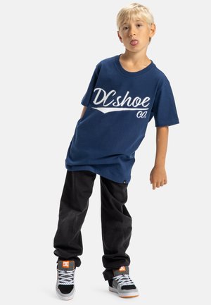 Granatowa bawełniana koszulka z białym logo "DC shoe Co.", zestawiona z czarnymi spodniami i wielokolorowymi sneakersami z szarymi, pomarańczowymi i białymi akcentami.