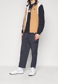 Vaaleanruskea ja tummansininen vetoketjullinen takki valkoisin yksityiskohdin; päällä musta graafinen t-paita; harmaat housut; valkoiset Nike-tennarit mustin yksityiskohdin.