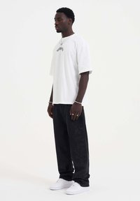 White cotton t-shirt with short sleeves, paired with loose black jeans featuring a subtle floral pattern, and white sneakers.