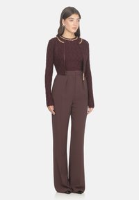 Chaqueta texturizada burdeos con mangas largas y detalle de cadena dorada, combinada con pantalones de pierna ancha de cintura alta en color a juego.