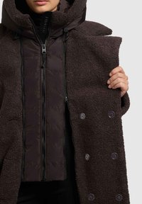 Tumepruun väliskorpus tekstuurse fliisviimistlusega, sisemine vooder suletava tõmblukuga siledas, tumedamas toonis ning läbipaistvad nööbikinnitused.