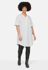 Witte tuniek met korte mouwen en een V-hals, gecombineerd met zwarte leggings en spijkerlaarzen met studs. Glad weefsel en een ontspannen pasvorm.