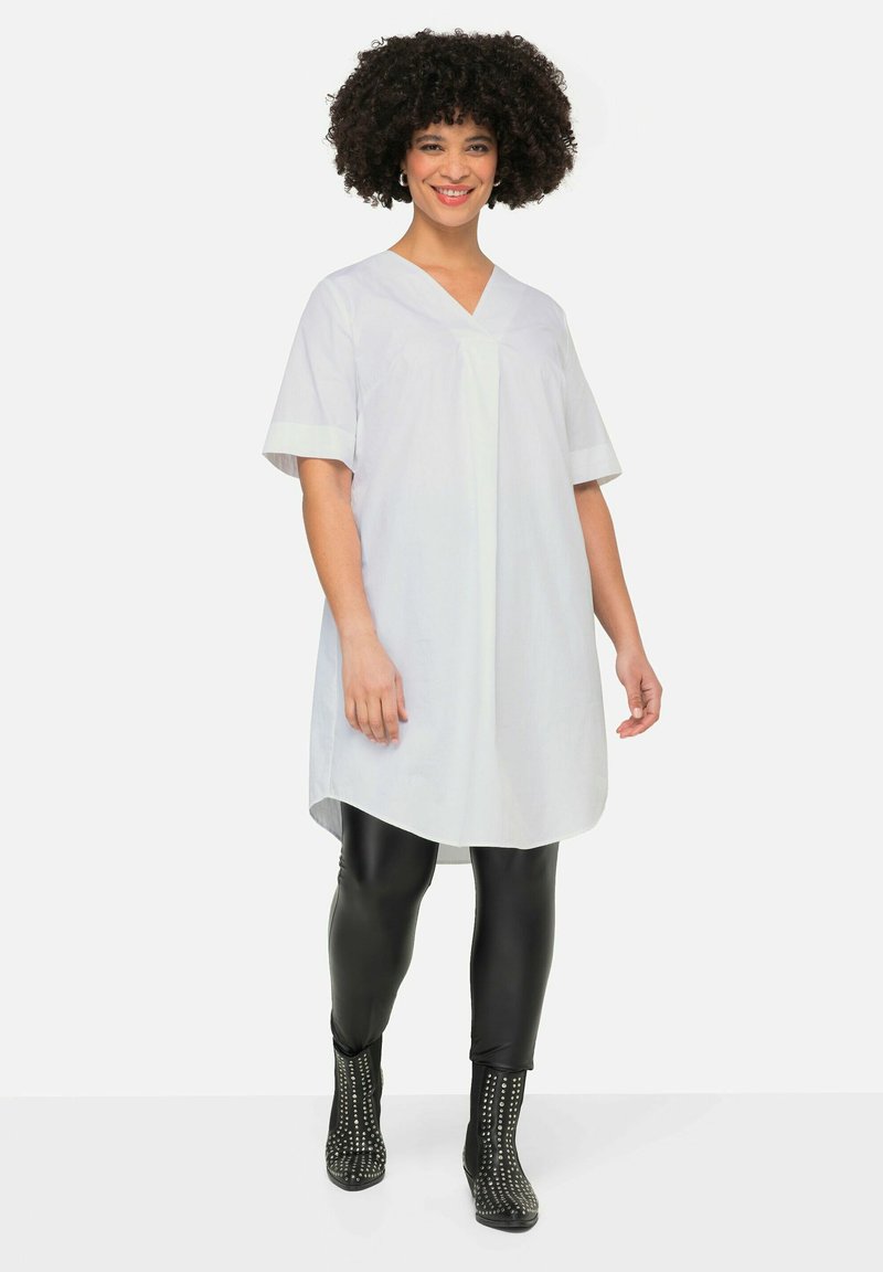 Witte tuniek met korte mouwen en een V-hals, gecombineerd met zwarte leggings en spijkerlaarzen met studs. Glad weefsel en een ontspannen pasvorm.