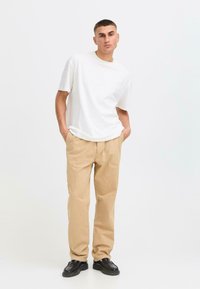 White short-sleeve T-shirt, beige tailored trousers, and black shoes. Plain textures, relaxed fit, and minimal design elements.