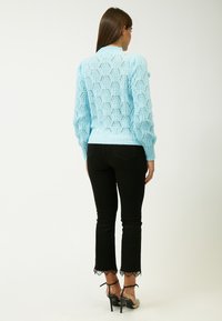 Maglione lavorato a maglia blu chiaro con un motivo testurizzato, polsini e orlo a costine. Abbinato a pantaloni neri a zampa d'elefante con rifiniture in pizzo.