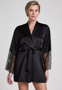 Raso nero con pizzo sui maniche. Presenta un design avvolgente, chiusura con cintura e una texture liscia.
