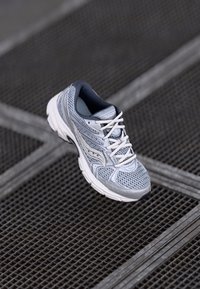 Scarpa sportiva grigia realizzata in mesh e materiali sintetici, con tomaia traspirante, collo imbottito e lacci bianchi. Suola in gomma con battistrada.
