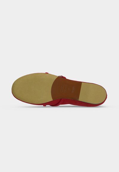 Vue de la semelle d’une sandale plate rouge avec une semelle extérieure lisse marron clair et marron, montrant les marquages de taille et de matériau au niveau du talon.