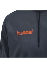 Sweat à capuche bleu marine en tissu texturé, avec un logo "hummel" orange sur la poitrine, et dispose d'un cordon de serrage à la capuche.