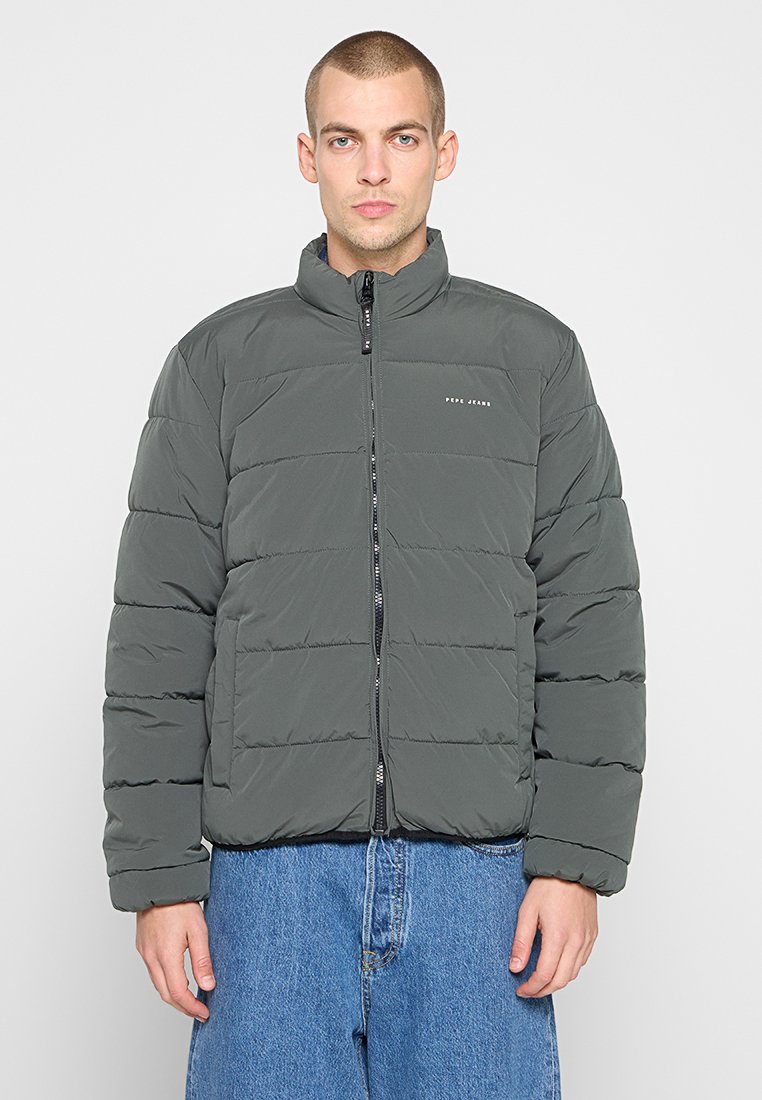 Chaqueta acolchada en gris oscuro con un alto cuello, costuras horizontales, cierre con cremallera frontal y un logo en el lado izquierdo del pecho. Diseño texturado y aislante.