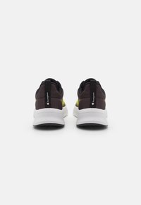 Mørkebrun sneakers med gule aksenter, strukturert stoffoverdel, polstret krage og hvit gummisåle med svart grep.