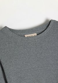 Szara, prążkowana koszulka z okrągłym dekoltem. Wewnątrz kołnierza widoczna metka wskazująca rozmiar S. Gładka textura i lekki materiał.