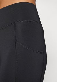 Czarne legginsy sportowe z wysokim stanem, z teksturowanym przeszyciem oraz boczną kieszenią po prawej stronie. Gładka wykończenie materiału.