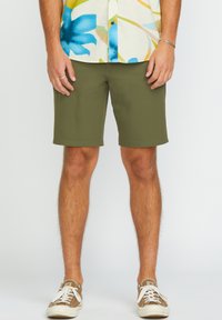 Shorts vert olive en tissu léger, avec une coupe droite et un ourlet. Associés à des baskets marron décontractées.