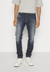 Mörkblå denimjeans med slim fit, med lätt slitning, kontrasterande sömmar och femficksdesign. Bärs med vita sneakers.