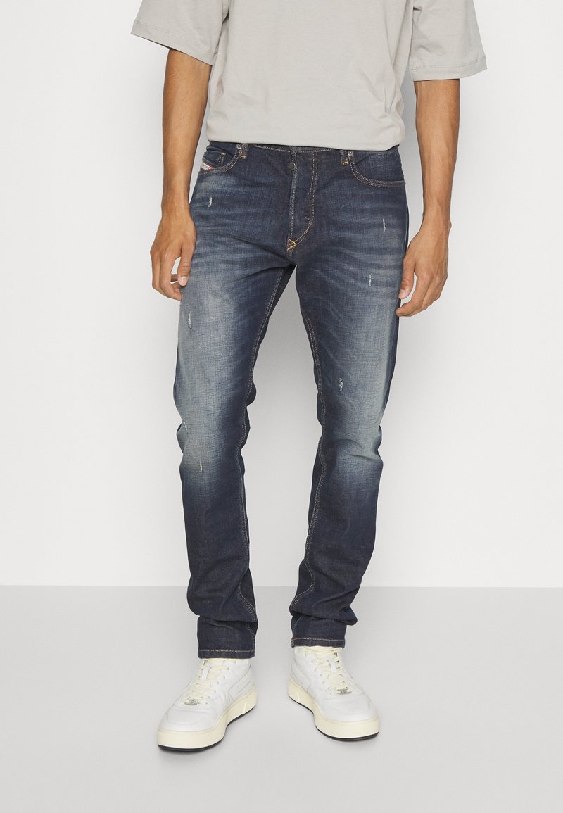 Mörkblå denimjeans med slim fit, med lätt slitning, kontrasterande sömmar och femficksdesign. Bärs med vita sneakers.