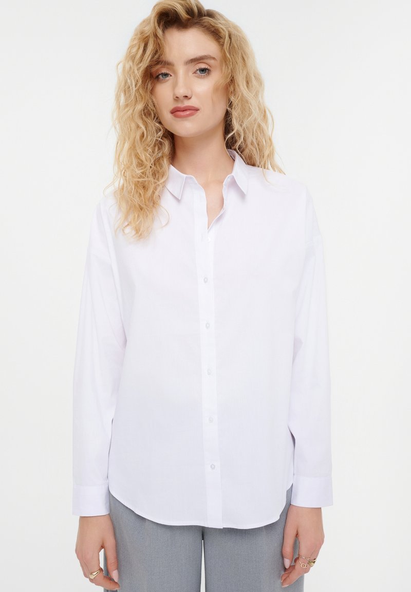 White button-up shirt with long sleeves, a classic collar, and a relaxed fit. Smooth texture with visible buttons down the front.