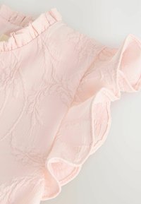 Hellrosa Stoff mit einem dezenten floralen Jacquardmuster und gerafften Kanten, in Nahaufnahme vor neutralem Hintergrund gezeigt.