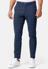 Mørkeblå ternede bukser lavet af vævet stof med slim fit. Har et hvidt rutenetmønster og en flad front med knaplukning.
