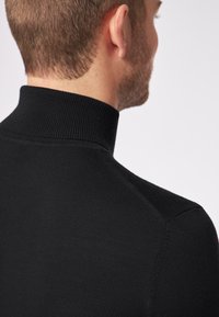 Schwarzer gerippter Rollkragenpullover, Nahaufnahme, die den hohen Kragen und die glatte Textur des gestrickten Stoffs am Rücken hervorhebt.