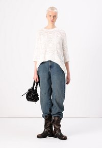 Hvit, strikket genser med geometrisk mønster, kombinert med løse blå denimjeans. En svart håndveske og brune støvler til knærne fullfører antrekket.
