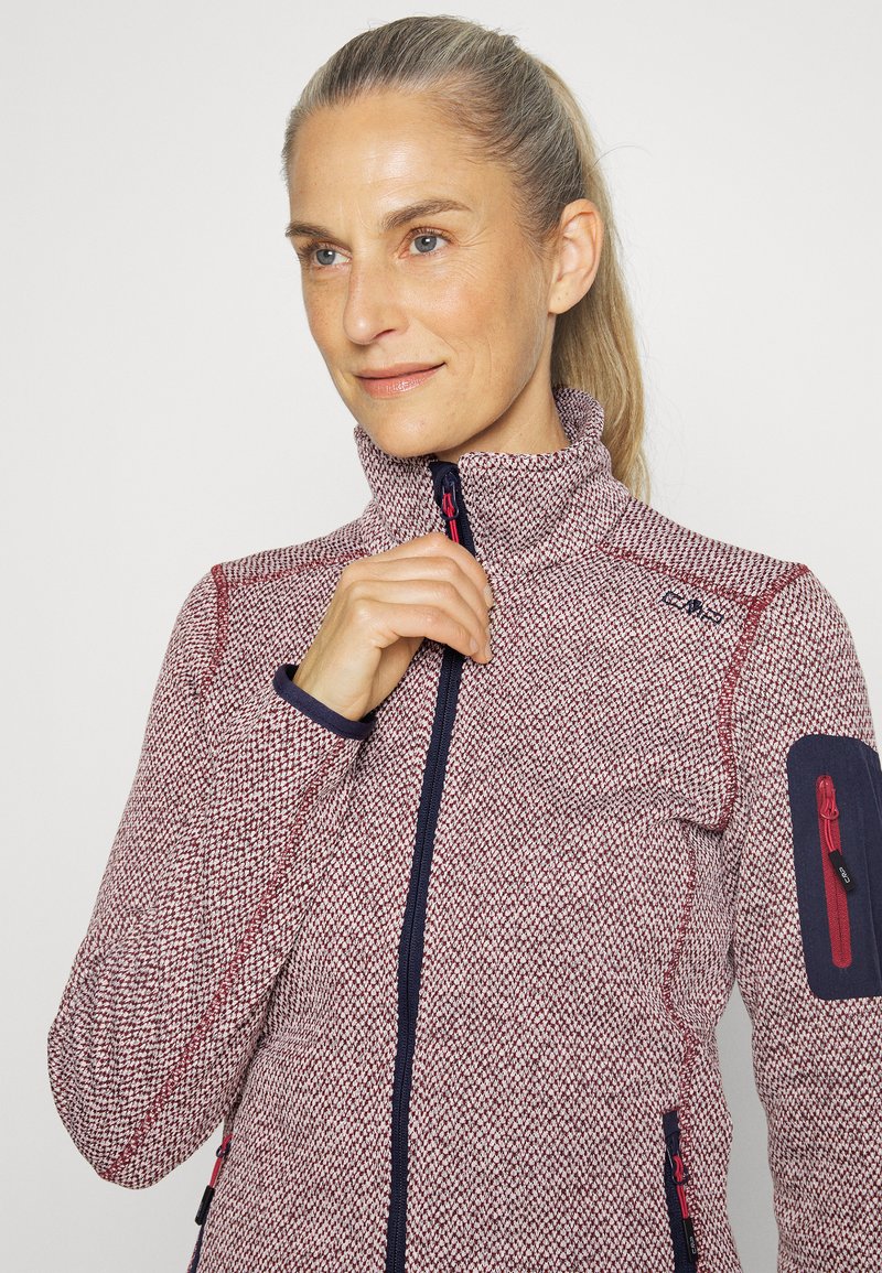 Giacca in pile con un motivo testurizzato in rosso e bianco, colletto alto, tasche con zip e dettagli blu navy su polsini e braccio.