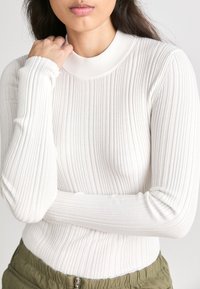 Hvit ribbet langermet topp med høy hals, glatt tekstur, tettsittende silhuett og slim fit, kombinert med olivengrønne bukser.