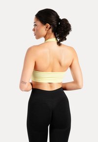 Gul ribbad kort topp med halterneck-design, kombinerad med svart högmidjade leggings. Slät textur och tajt passform.