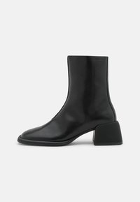 Svart läderankelboots med spetsig tå och en kraftig, geometrisk klack. Slät textur med minimal detaljering.