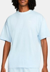 Ljusblå t-shirt med korta ärmar i bomull, med en rundad halsringning och en liten vit Nike-logotyp på vänster bröst. Slät textur.