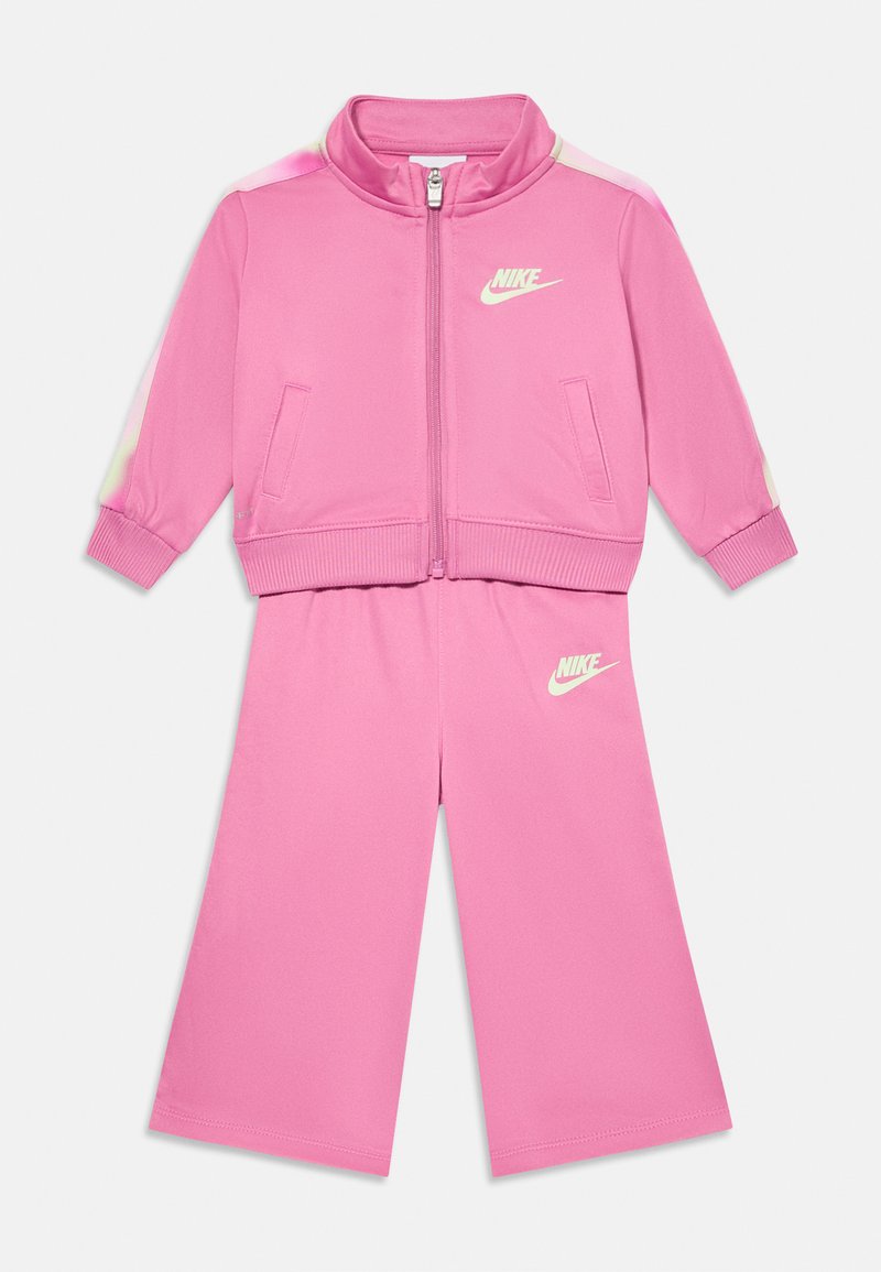 Completo tuta rosa composto da giacca con zip e colletto e pantaloni larghi coordinati. Realizzato in tessuto liscio con dettagli del logo Nike bianchi.