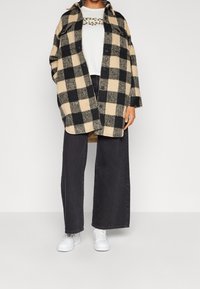 Černá a béžová kostkovaná vlněná bunda přes bílý tričko s grafikou, spárovaná s černými džíny s vysokým pasem a bílými teniskami.