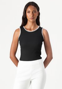 Top negro sin mangas con escote redondo, con costuras en zigzag blancas alrededor del cuello. Textura suave, diseño ajustado.