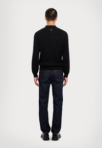 Maglione a coste nero con maniche lunghe, abbinato a jeans in denim blu scuro e scarpe nere, visto da dietro.