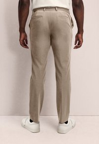Pantalones de corte beige con una textura suave, bolsillos traseros y cinturilla elástica, combinados con zapatillas blancas.