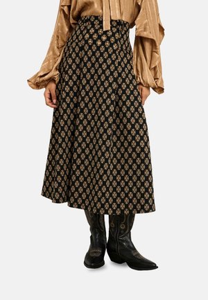 Mujer con falda midi negra con estampado floral en tono marrón claro, blusa dorada texturizada con mangas amplias y botas vaqueras negras bordadas.