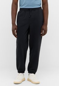 Schwarze Sweatpants mit elastischem Bund und Bündchen, die einen lässigen Schnitt und eine weiche Textur aufweisen. Tragen mit weißen Sneakers.