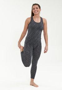 Mustikkasininen ja harmaaraidoitettu urheilupuku istuvalla muotoilulla, tanktop-tyylillä ja joustavalla kankaalla. Malli tekee seisovaa jalkavenytystä.