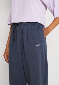 Nike byxor i mörkblått, med dragsko i midjan, sidofickor och en glittrande silverlogotyp broderad på vänster höft.