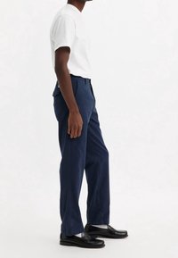 Pantalon bleu marine à coupe droite, en coton. Comprend des poches latérales et une texture lisse, associé à des mocassins noirs. T-shirt blanc.