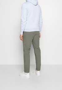 Sudadera con capucha azul claro, pantalones verde oliva y zapatillas blancas. El conjunto presenta un corte holgado y un diseño minimalista sin patrones visibles.