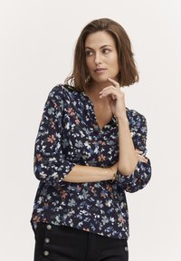 Blusa floreale navy con maniche a tre quarti, caratterizzata da una scollatura a V. Tessuto leggero con motivi floreali colorati e vestibilità comoda.