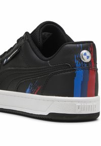 Čierne kožené tenisky s bielou podrážkou, s modrými a červenými akcentmi a logom BMW blízko päty. Textúrovaný povrch a polstrovaný golier.